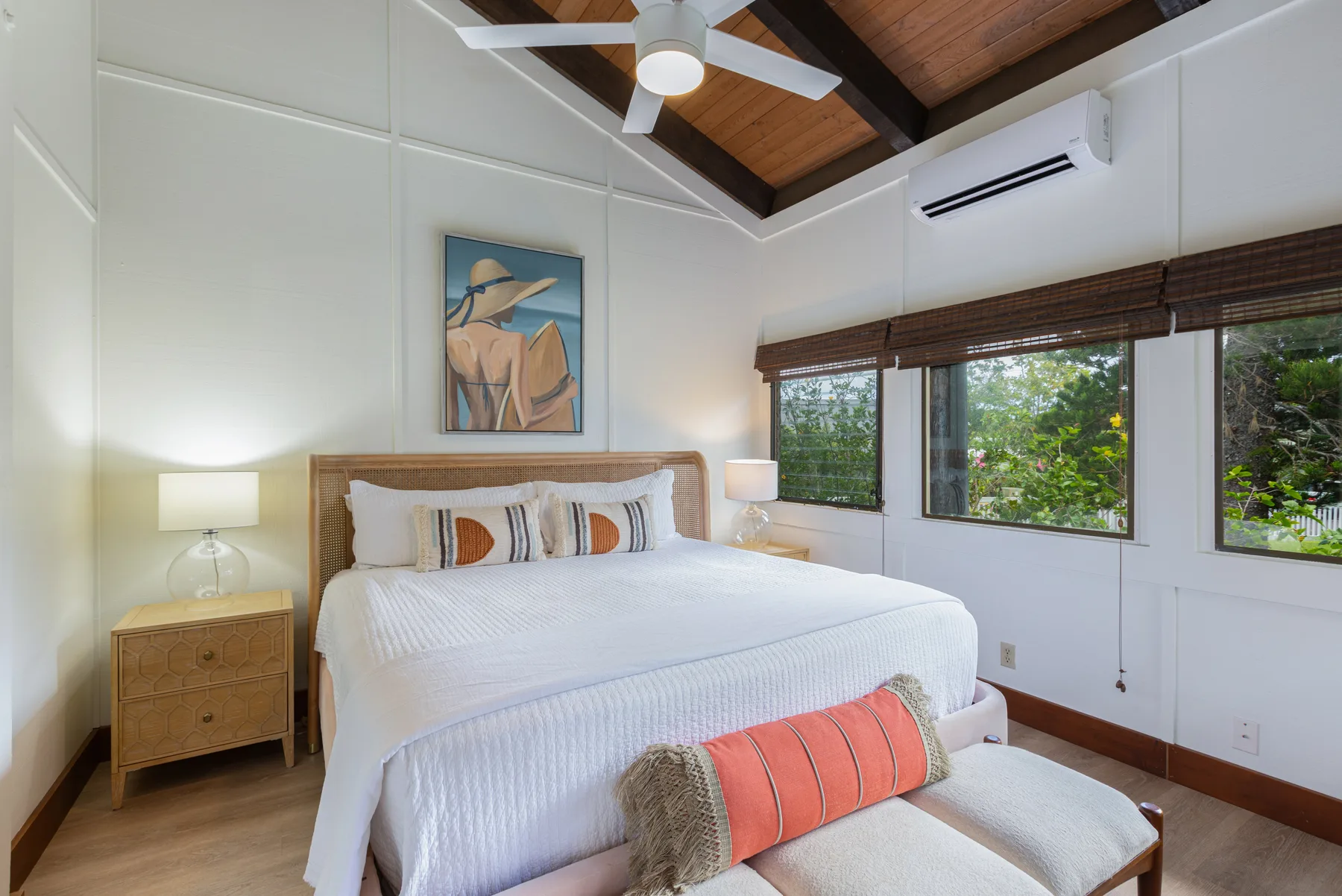 A bedroom with a neatly made bed and windows overlooking greenery.