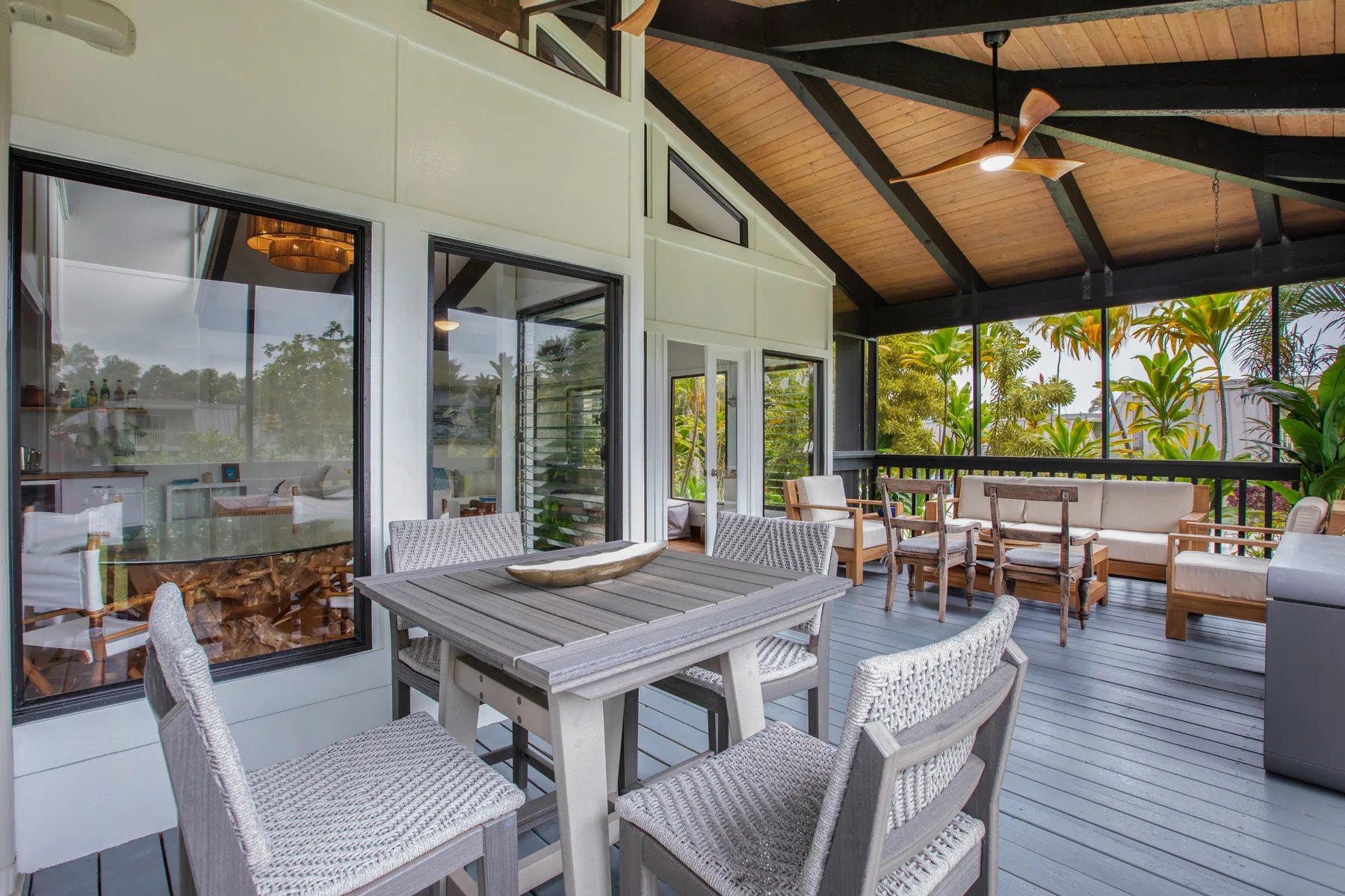 A covered outdoor dining area with a table and seating beside large windows.