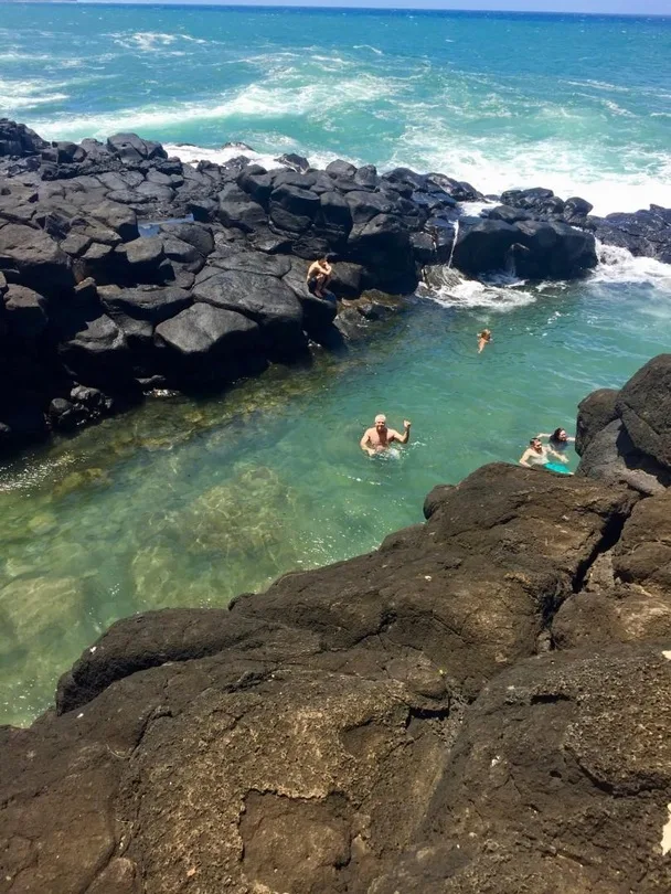 A natural ocean pool between dark rocks, with swimmers in the water.