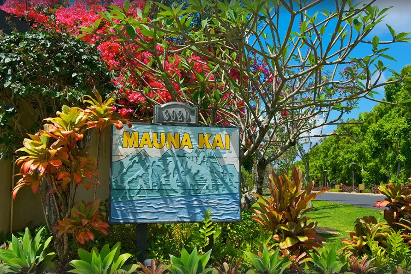 A garden sign reading “Mauna Kai” stands among tropical plants and trees.