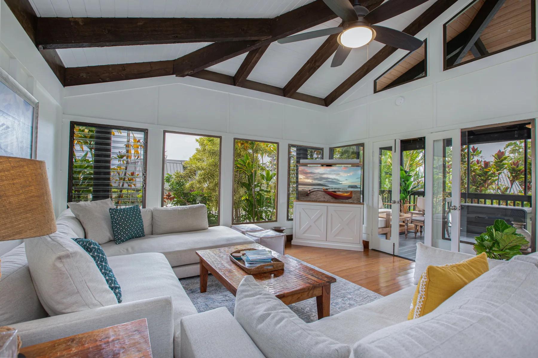 A bright living room with light-colored seating, a wooden coffee table, and large windows.