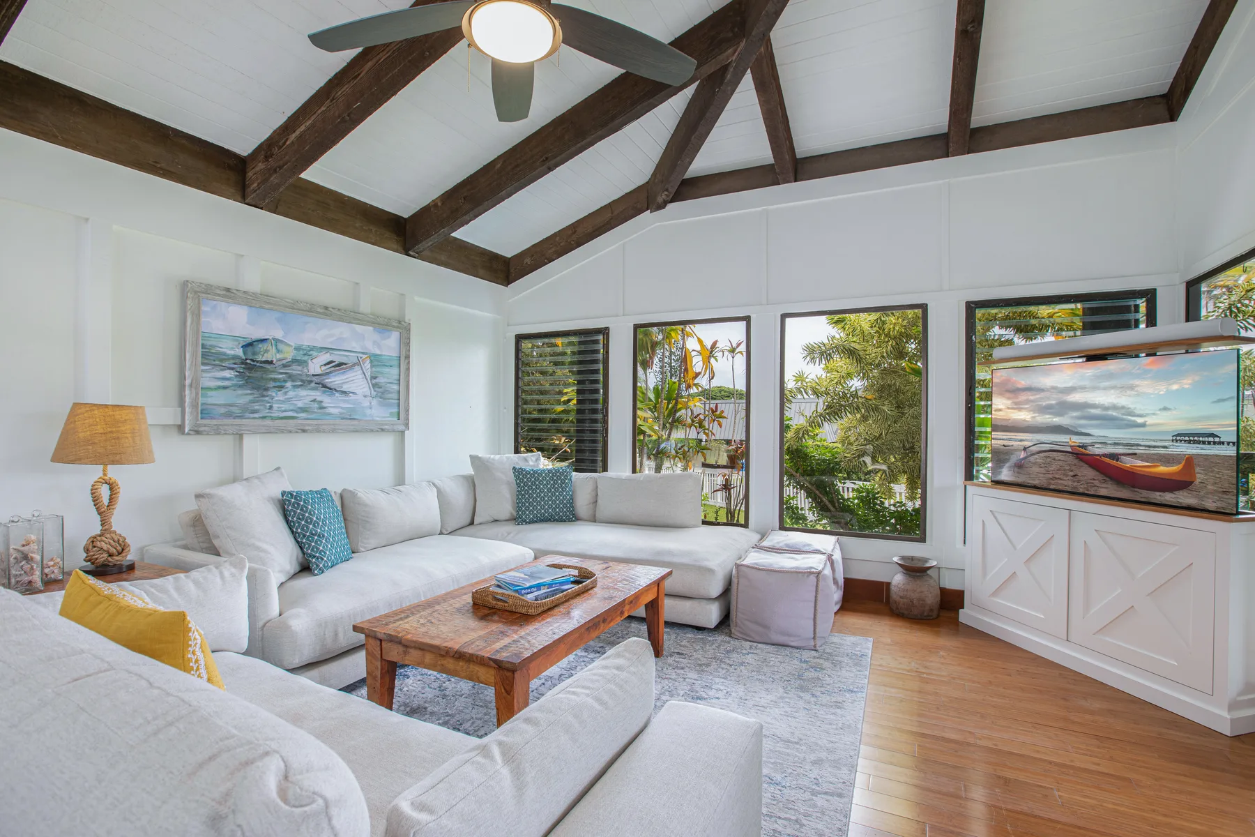 A bright living room with white seating, a wooden coffee table, and large windows.