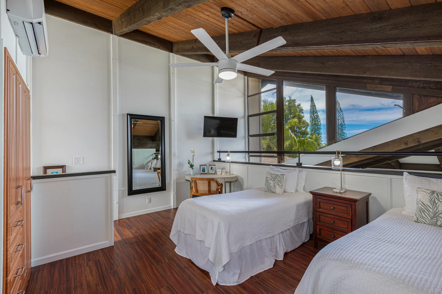 A bedroom with two beds, large windows, and a ceiling fan.