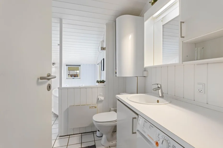 Un baño luminoso con lavabo, inodoro y paredes blancas con paneles.