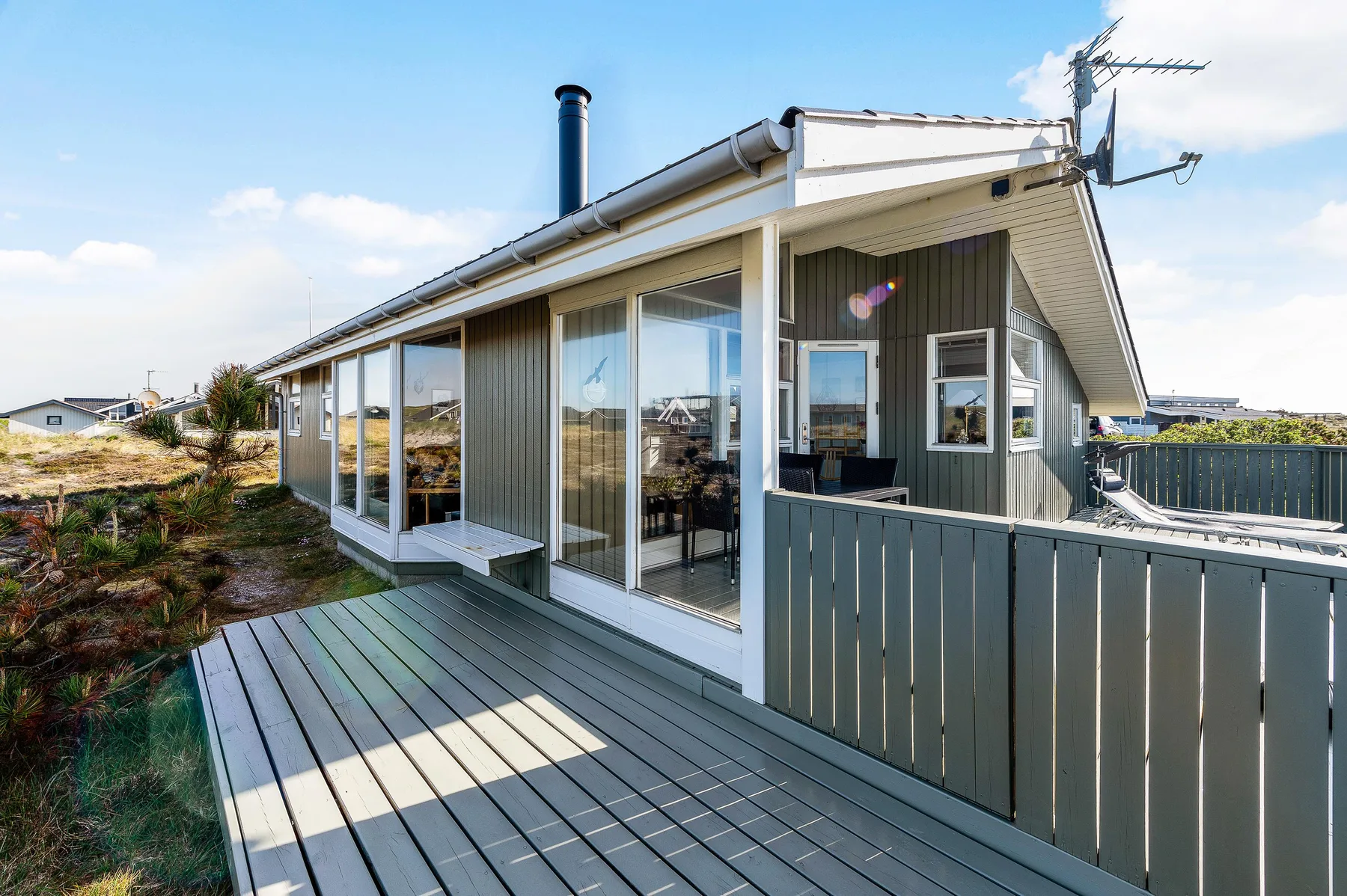 Exterior de una casa con una terraza de madera y grandes ventanales.