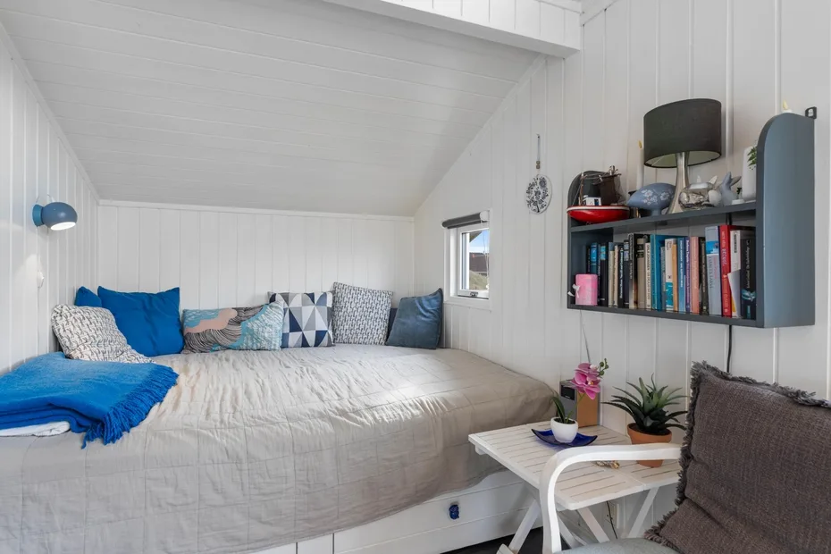 Un dormitorio luminoso con una cama, cojines de colores y una mesita auxiliar.
