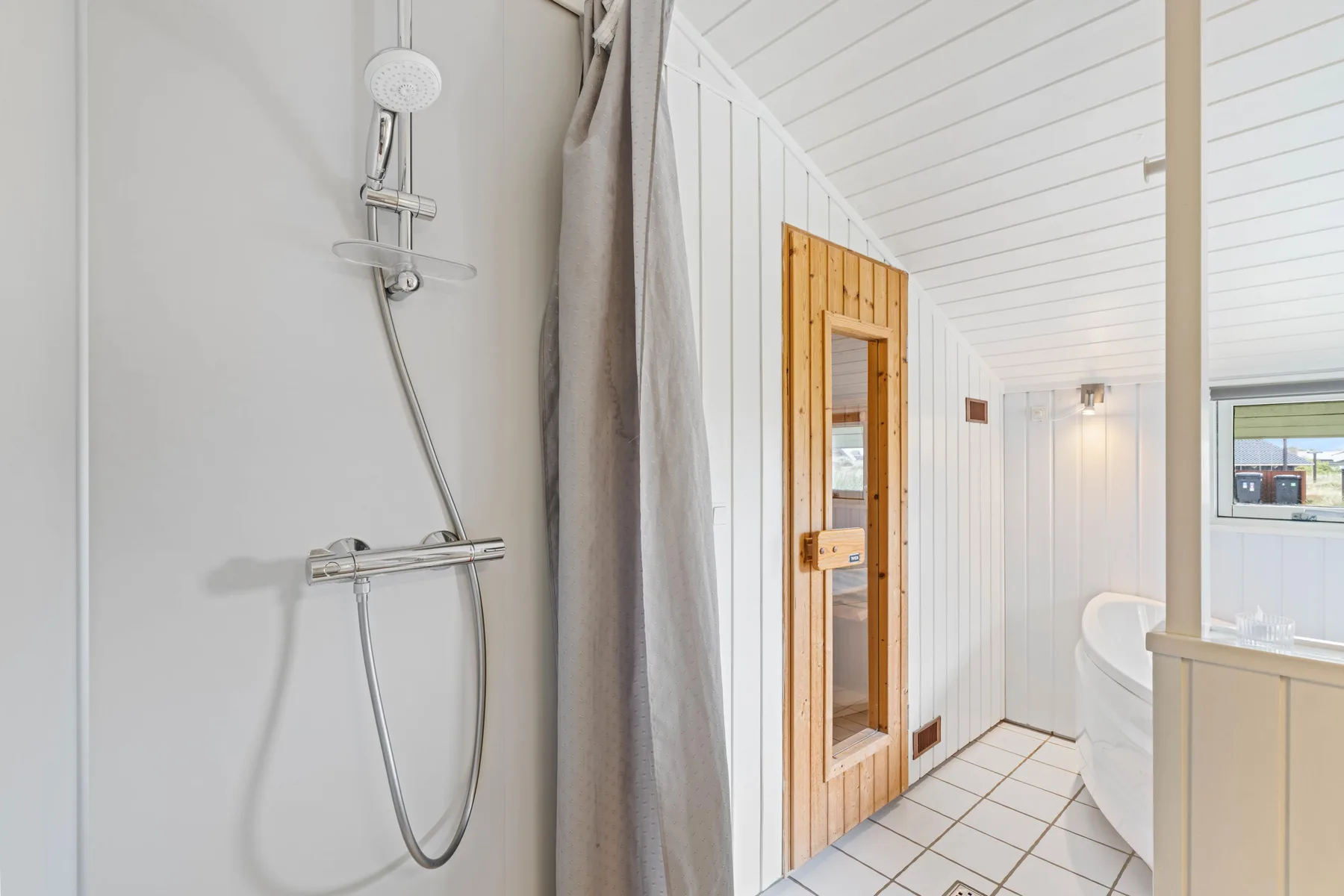 Un baño luminoso con ducha, bañera y una puerta de sauna de madera.
