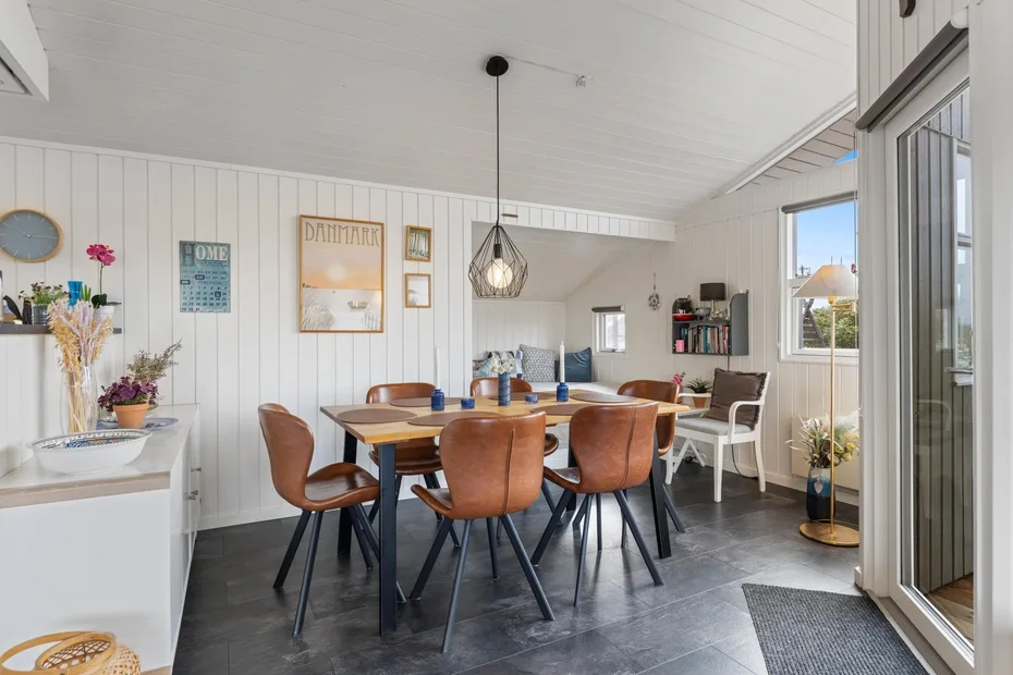 Un comedor luminoso con una mesa de madera y asientos junto a grandes ventanas.