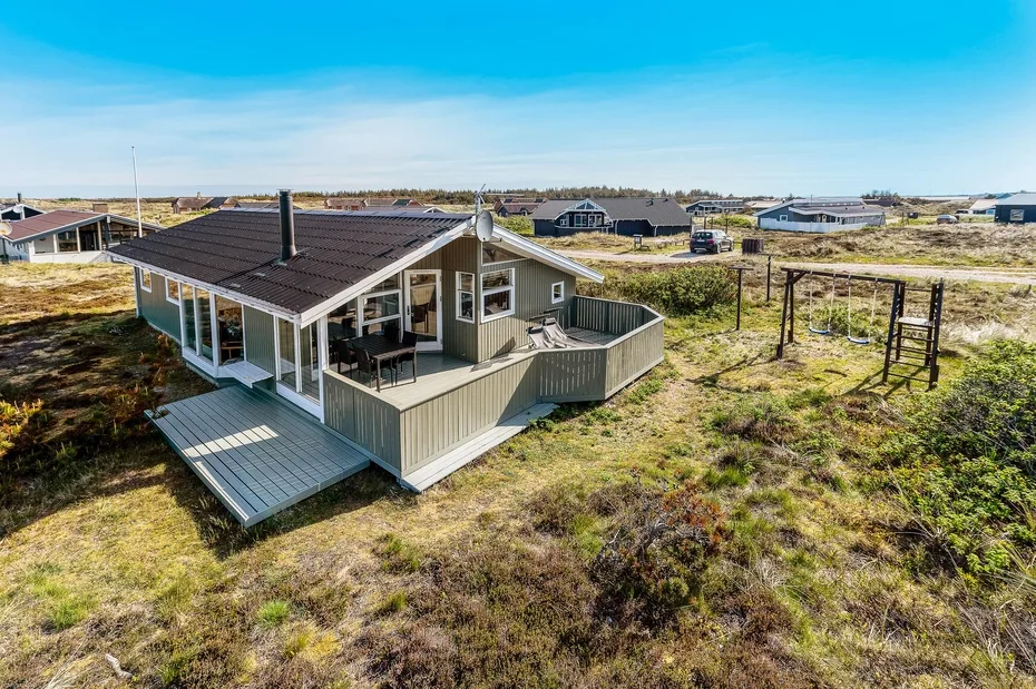 Una casa pequeña con una terraza elevada se encuentra en un paisaje abierto y cubierto de hierba.