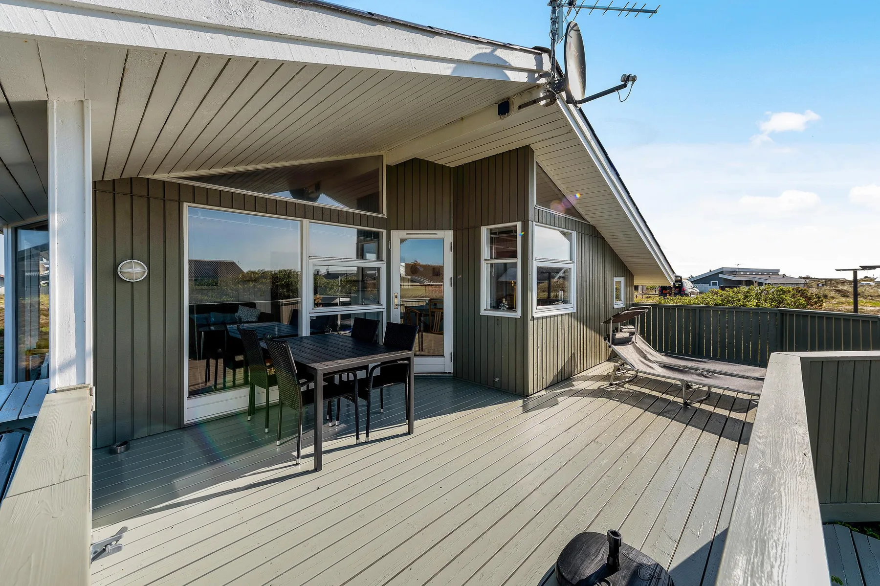 Una terraza de madera junto a una casa tiene asientos al aire libre y puertas corredizas de vidrio.