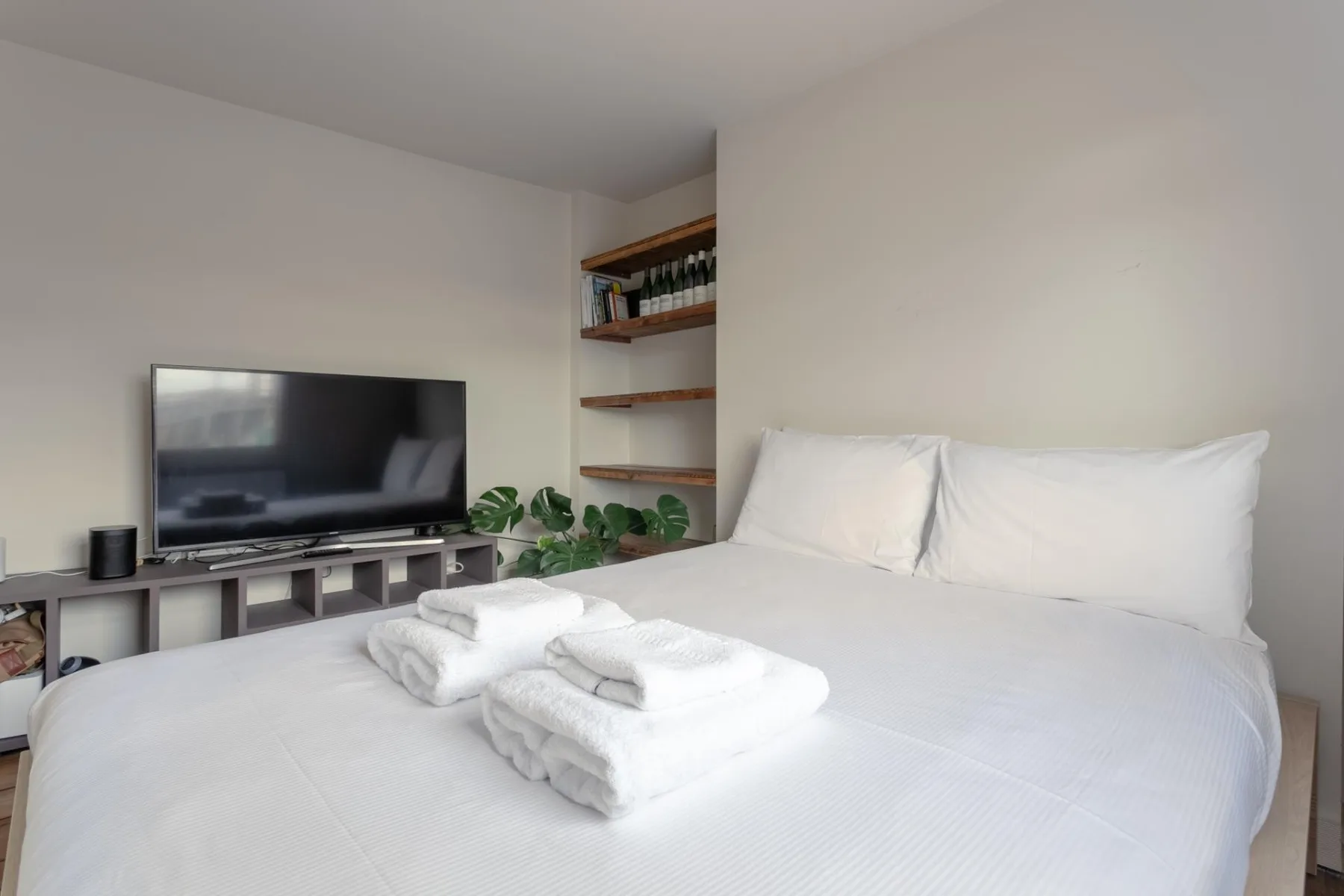 Un dormitorio con una cama blanca, toallas dobladas y un televisor sobre un mueble bajo.