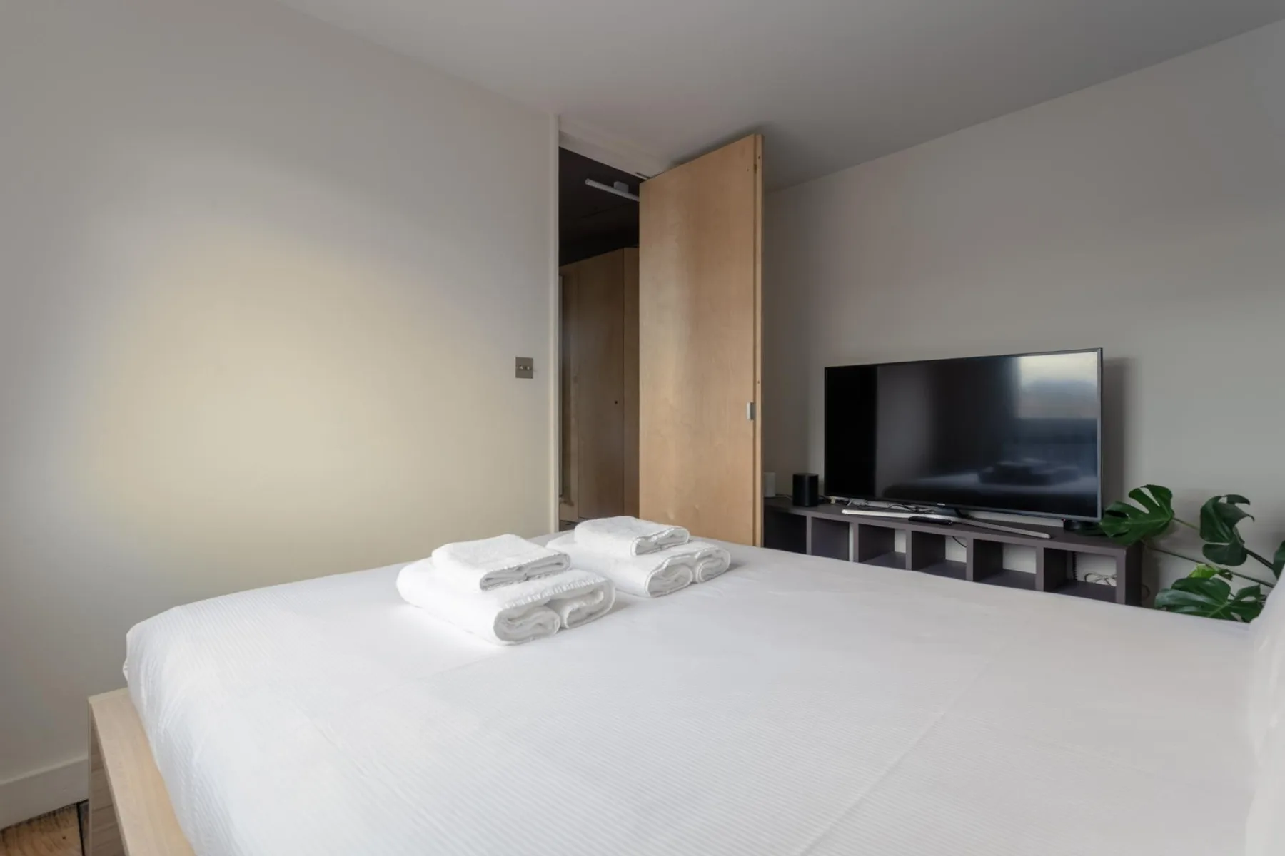 Un dormitorio luminoso con una cama tendida y un televisor sobre un mueble bajo.