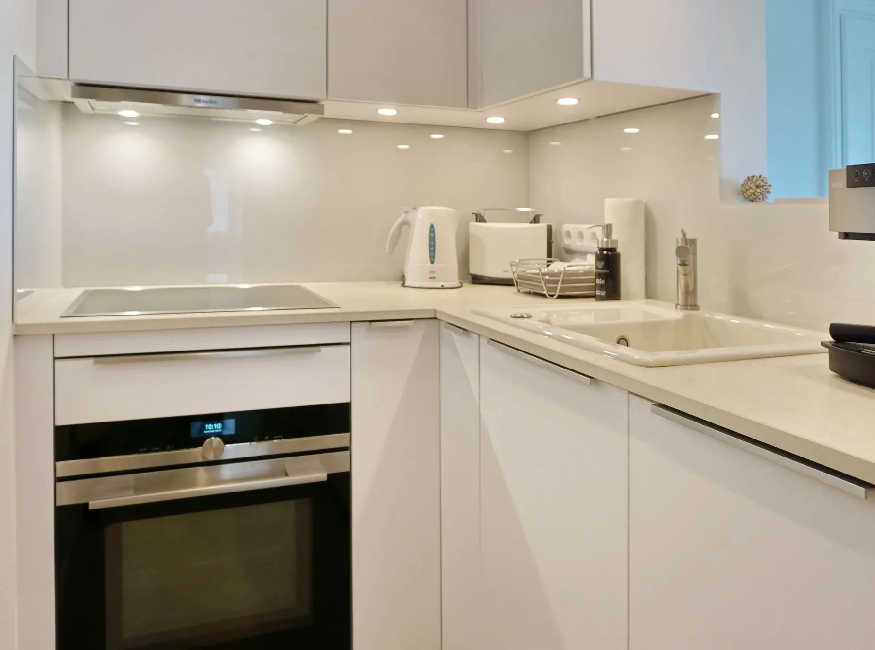 Una cocina moderna con gabinetes blancos, un horno empotrado y un fregadero en la encimera.