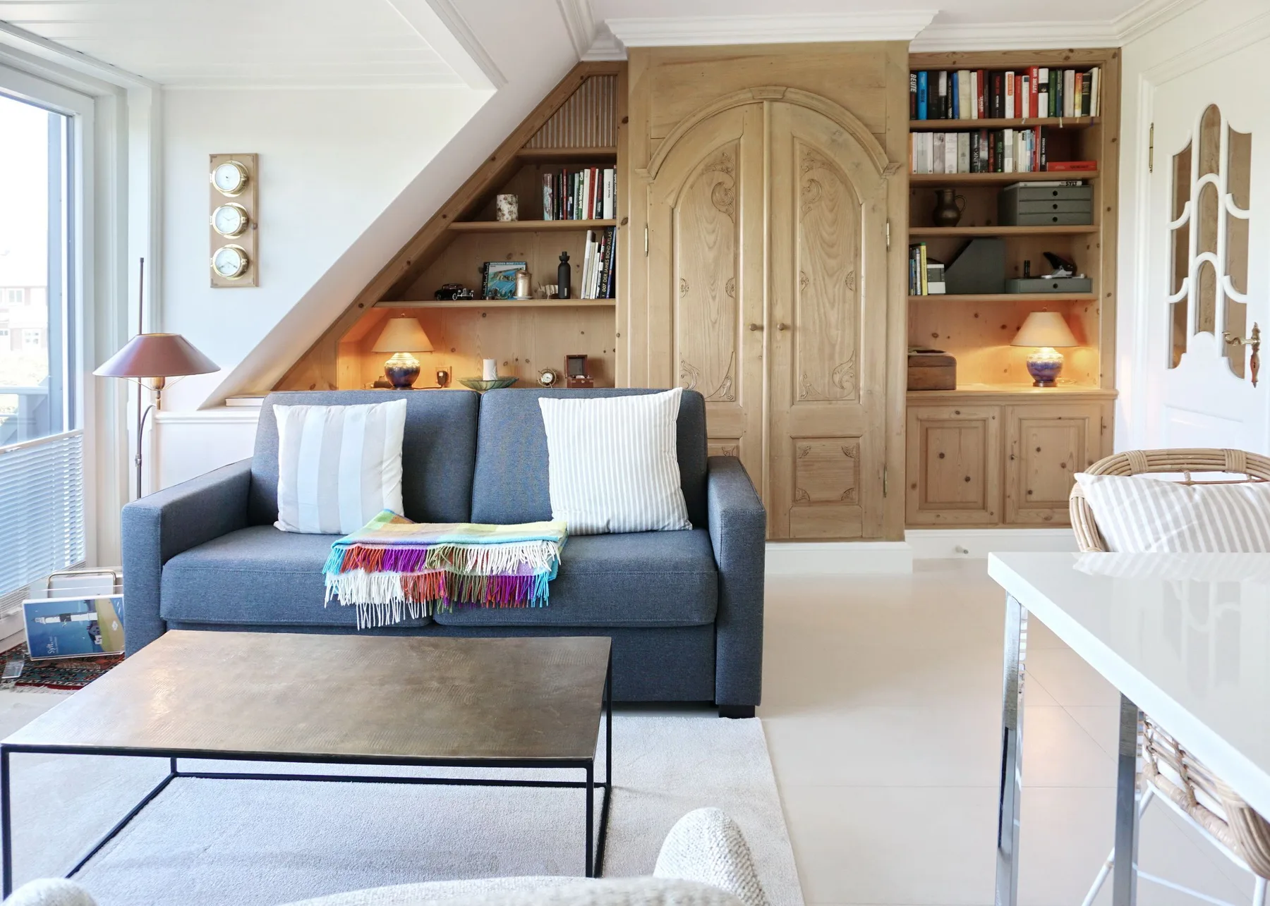 Una sala de estar luminosa con un sofá azul y estanterías de madera empotradas.