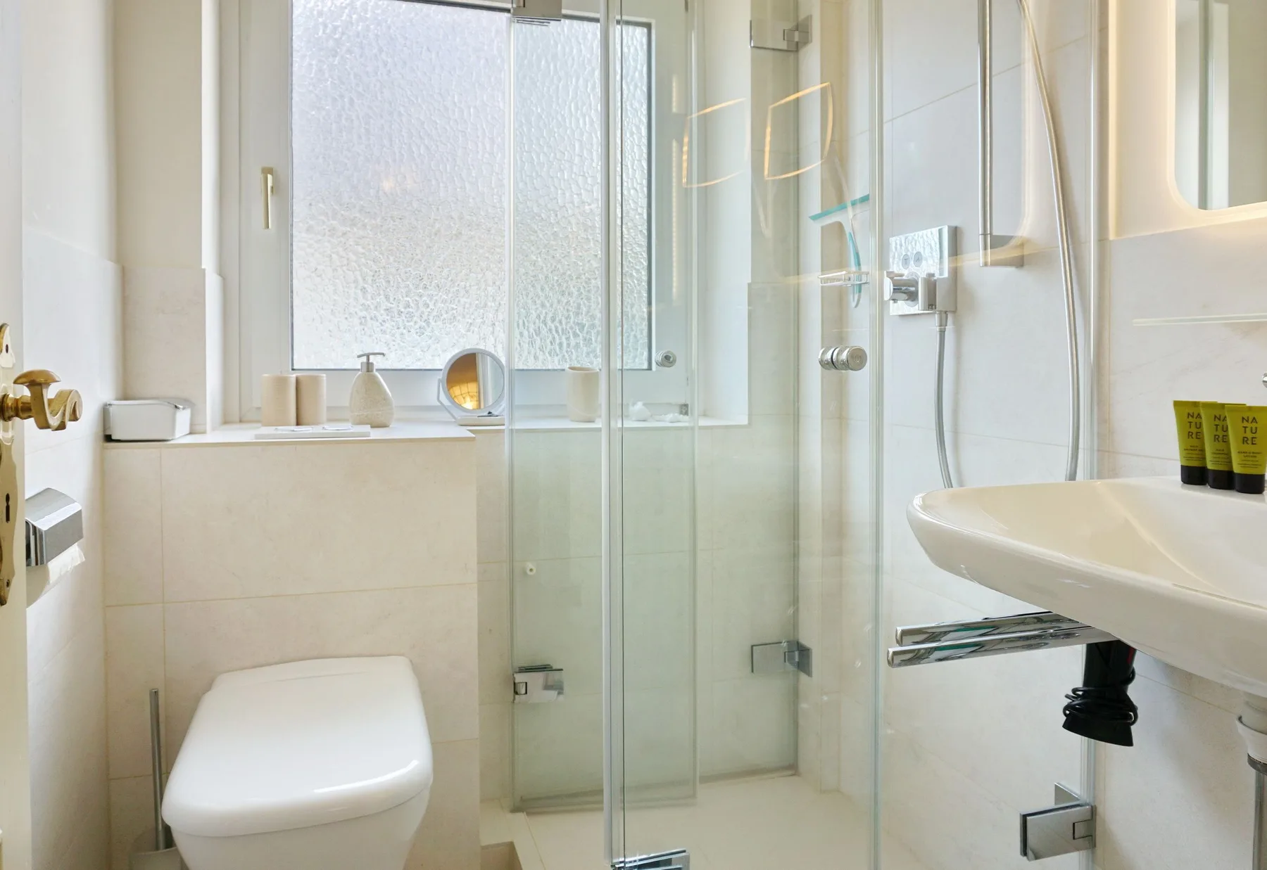 Un baño luminoso con ducha de vidrio, inodoro y lavabo de pared.