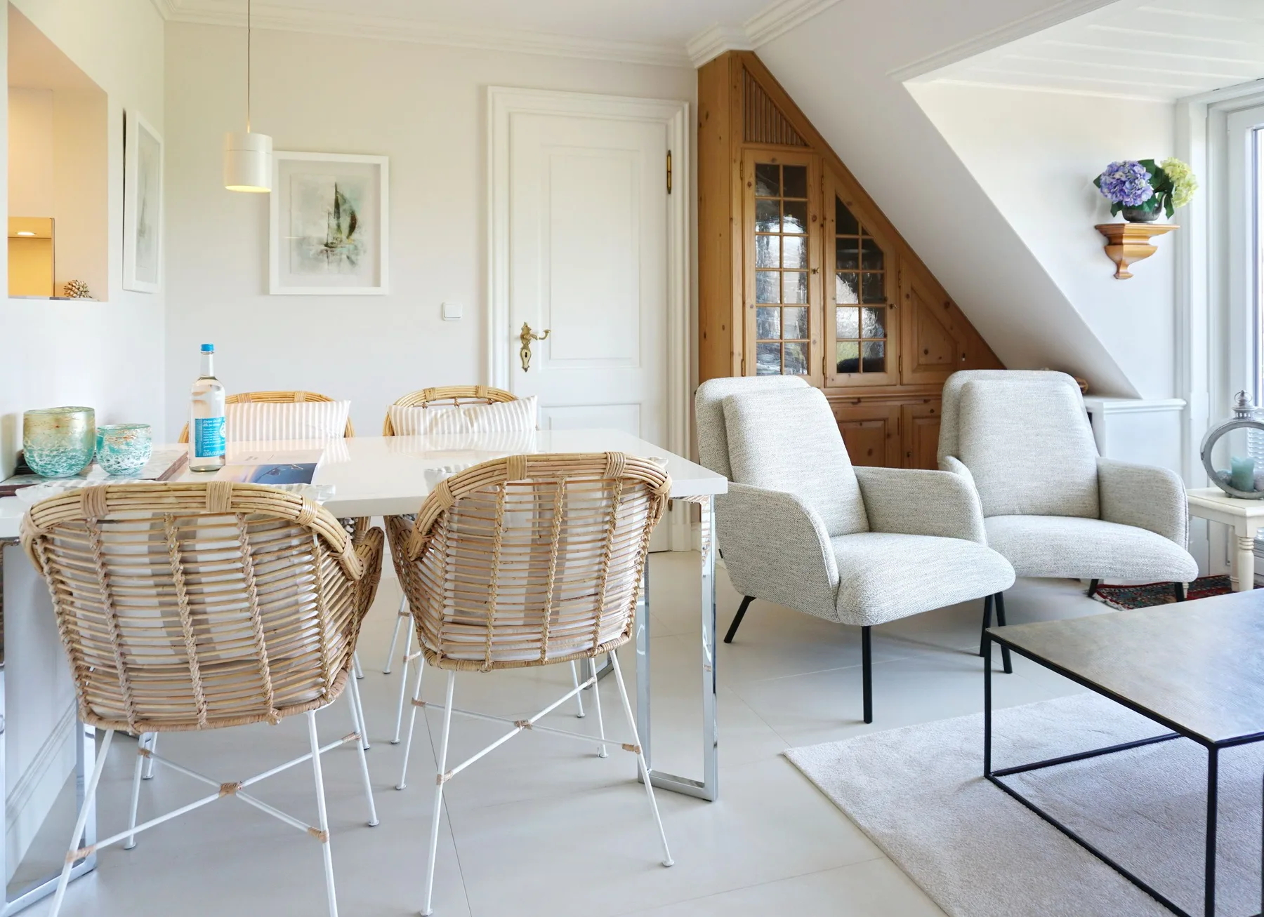 Una luminosa zona de comedor y estar con una mesa, asientos de mimbre y sillones claros.