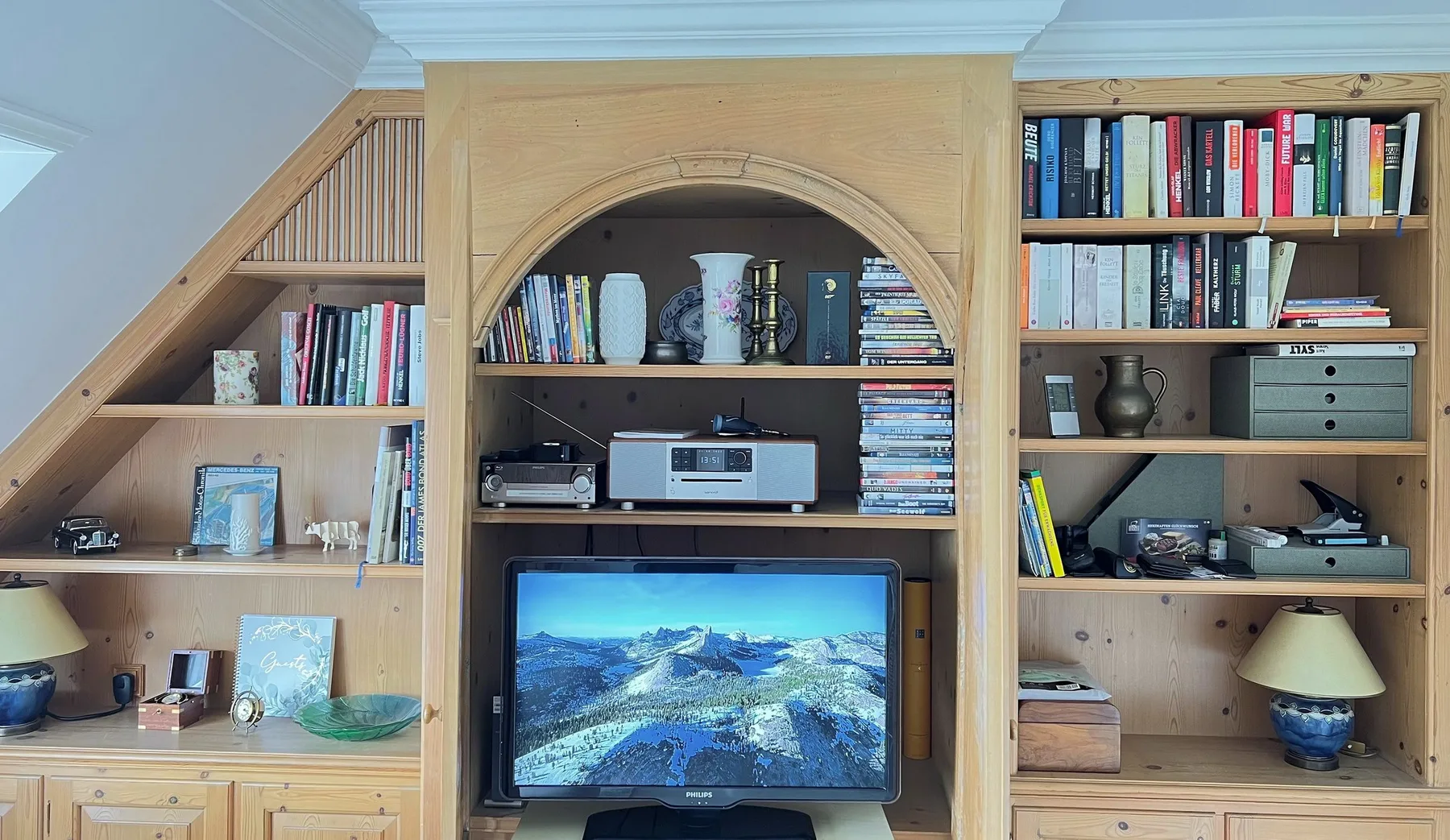 Una estantería empotrada de madera muestra libros, adornos y un televisor.