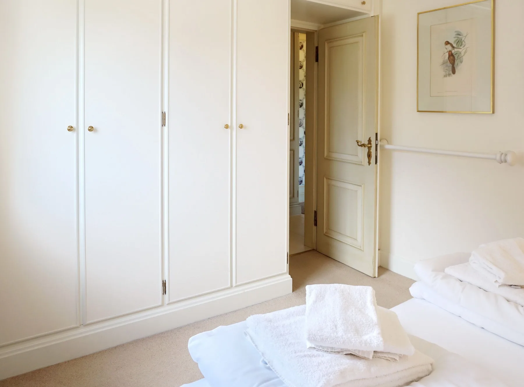 Un dormitorio luminoso con armarios blancos y ropa de cama doblada sobre la cama.