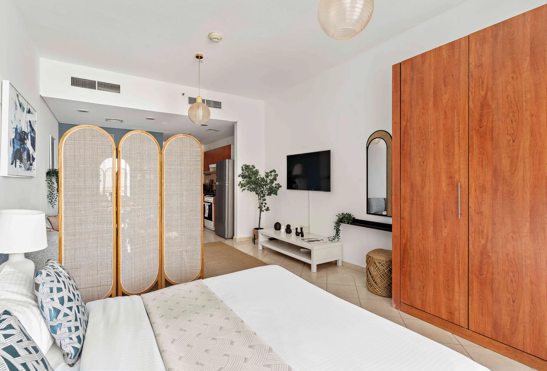 Un dormitorio luminoso con una cama, un armario de madera y un biombo tejido.