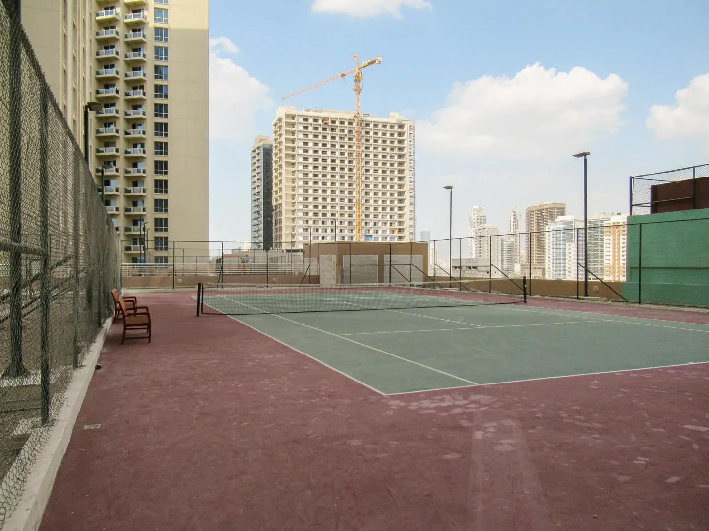 Una cancha de tenis al aire libre con superficie verde y edificios altos alrededor.