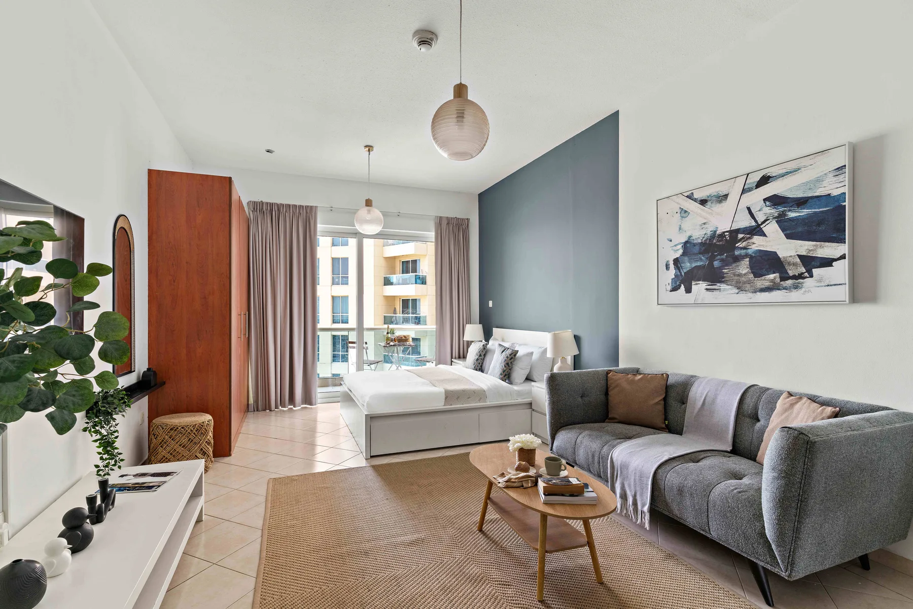 Estudio con cama, zona de estar y puertas de vidrio hacia el balcón.