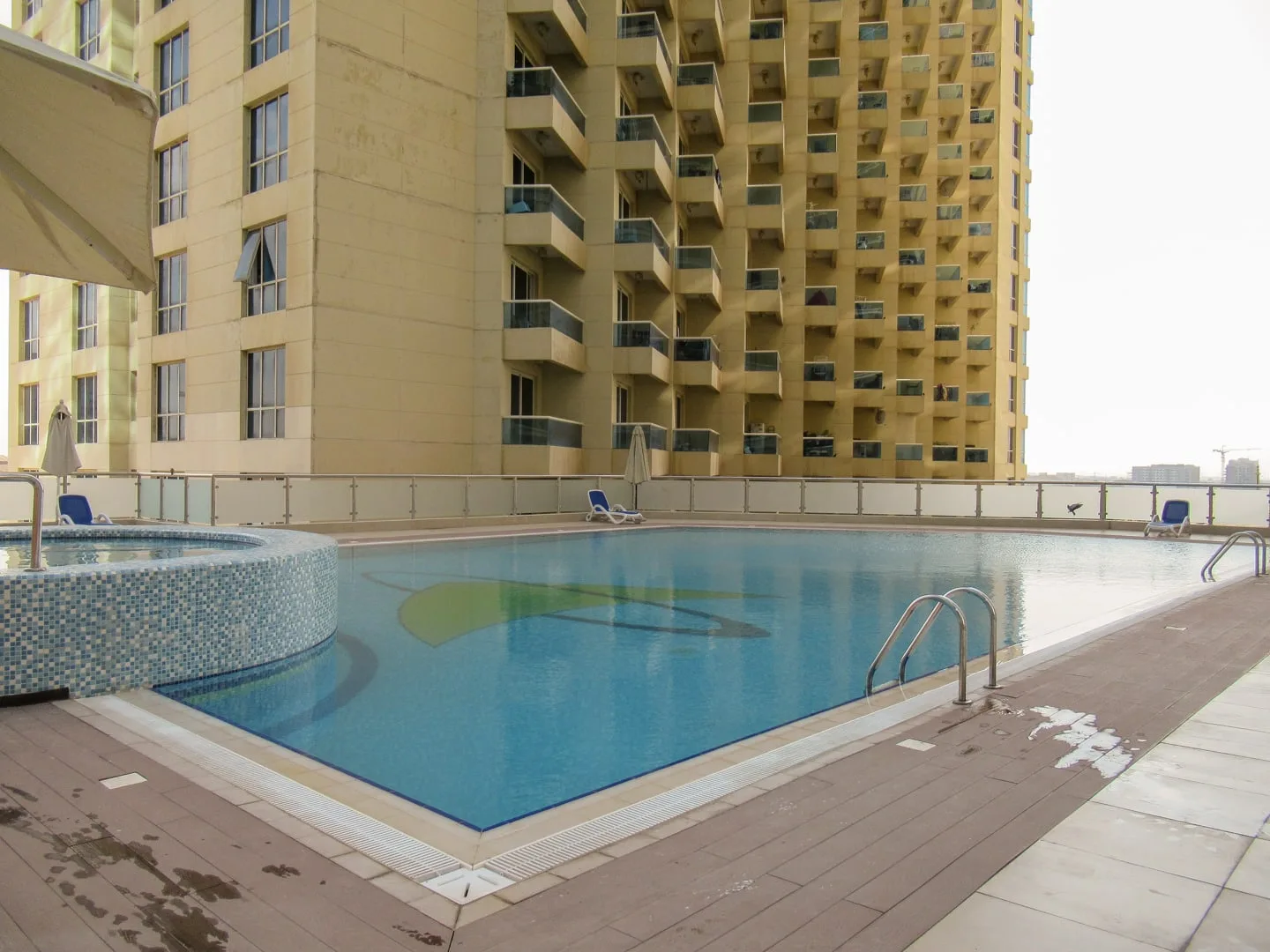 Una piscina en la azotea junto a un edificio alto, con tumbonas alrededor.