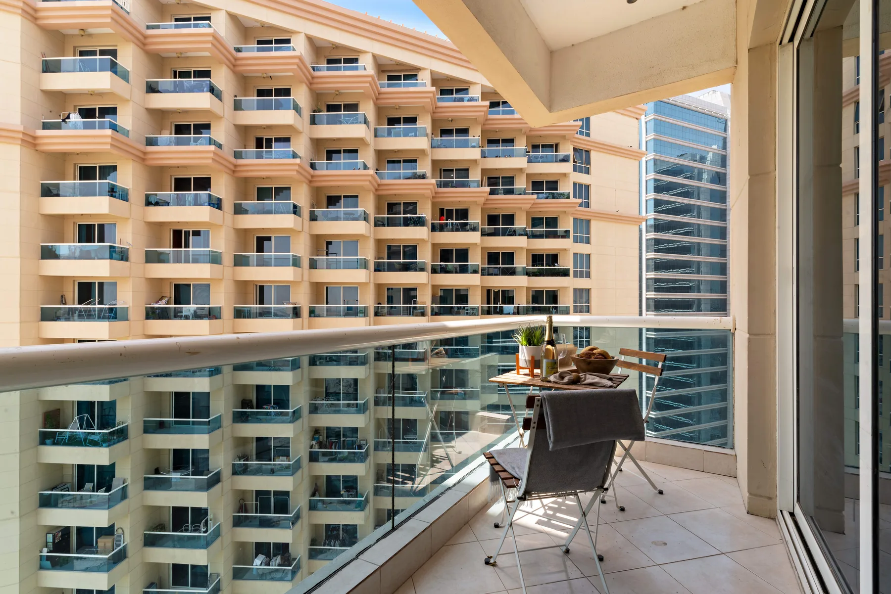 Un balcón con asientos y una mesa pequeña da a edificios de apartamentos cercanos.
