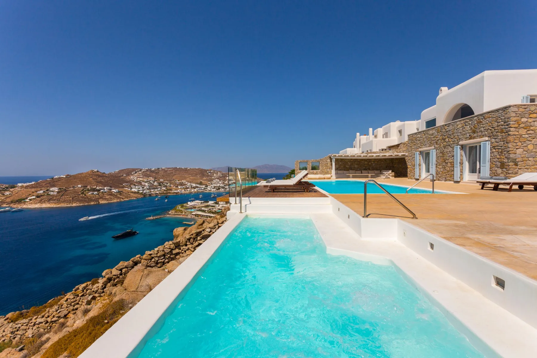 Una piscina turquesa tiene vistas al mar junto a un edificio con fachada de piedra.