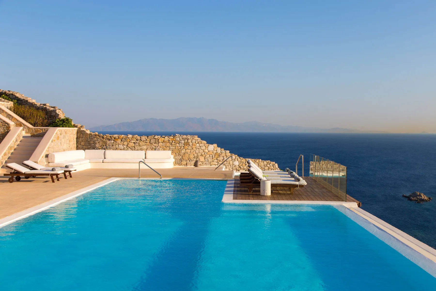 An outdoor swimming pool overlooks the sea beside a stone terrace.