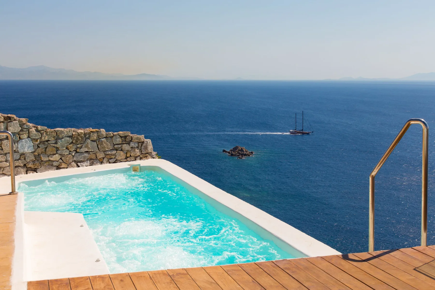 Una piscina mira al mar, con un velero visible en la distancia.