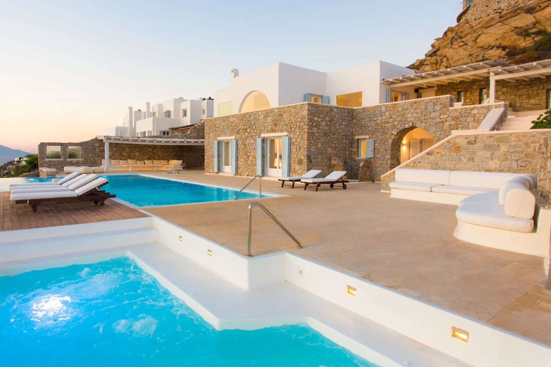Una piscina y una terraza contigua están junto a un edificio revestido de piedra.