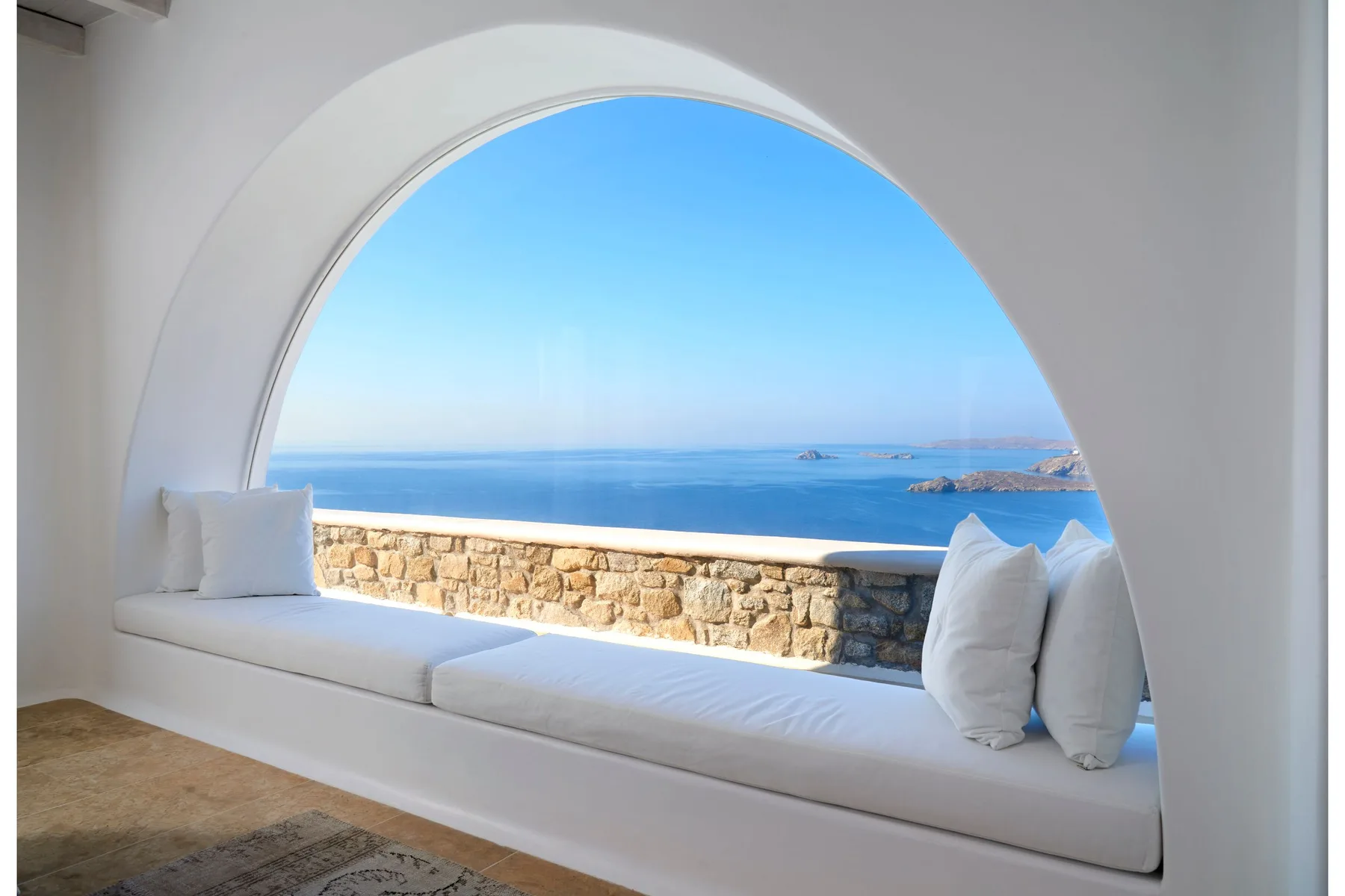 Una ventana curva enmarca una vista al mar sobre un asiento acolchado.