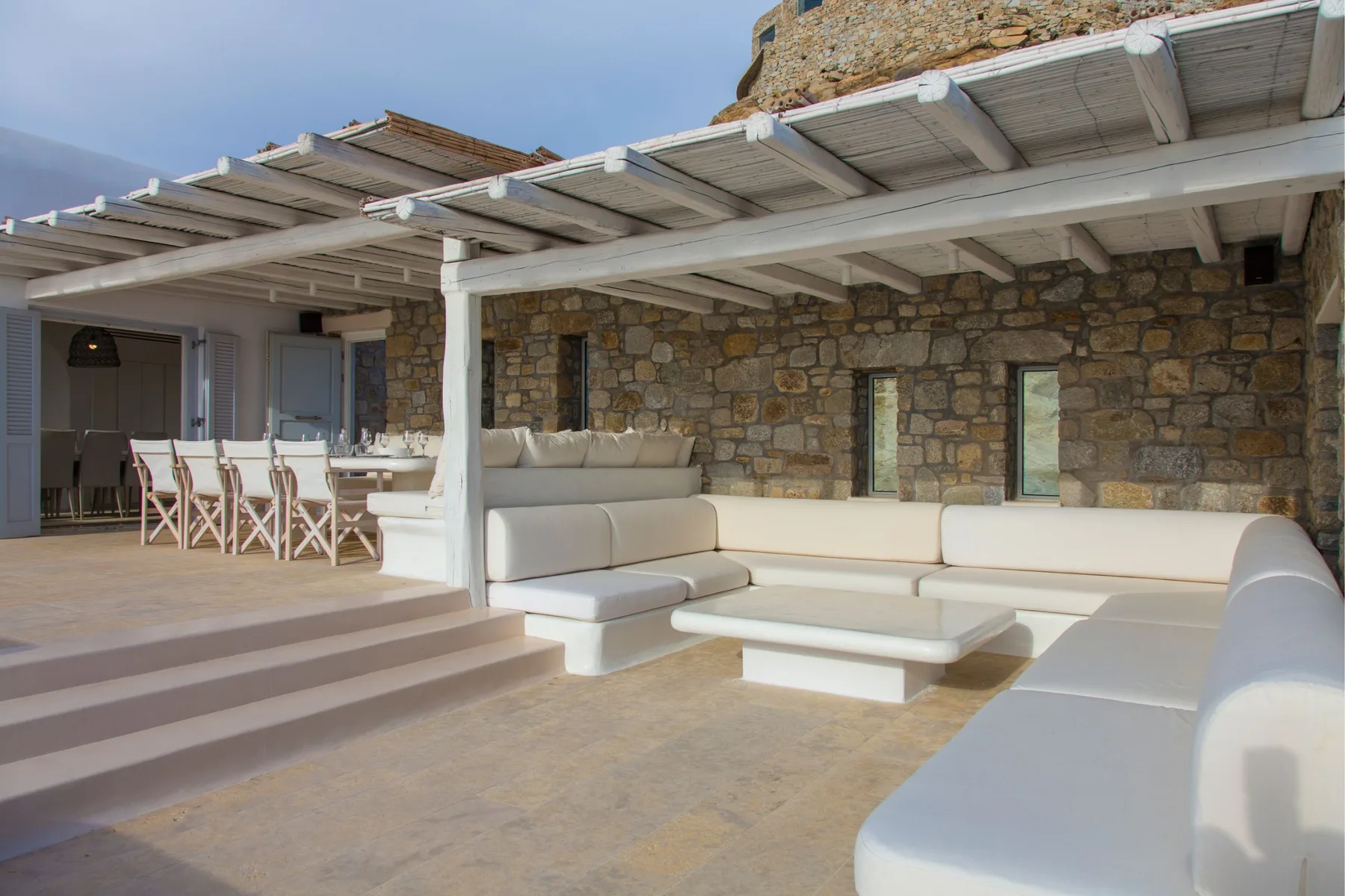 Zona de estar exterior con asientos integrados bajo una pérgola blanca.