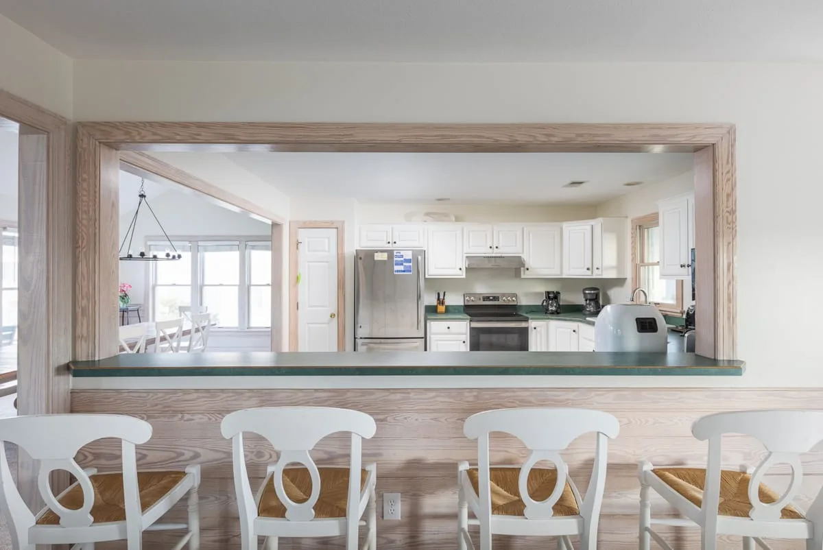 Una cocina se ve a través de una amplia abertura, con asientos junto a la barra.