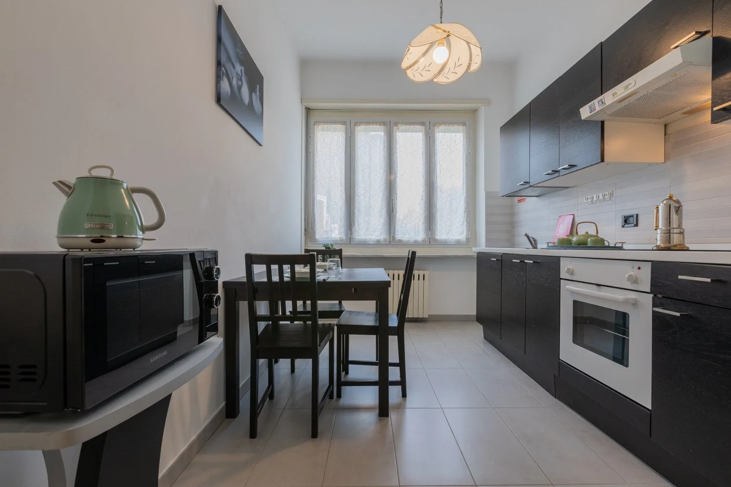 Una cocina estrecha con gabinetes oscuros, una mesa de comedor y una ventana al fondo.