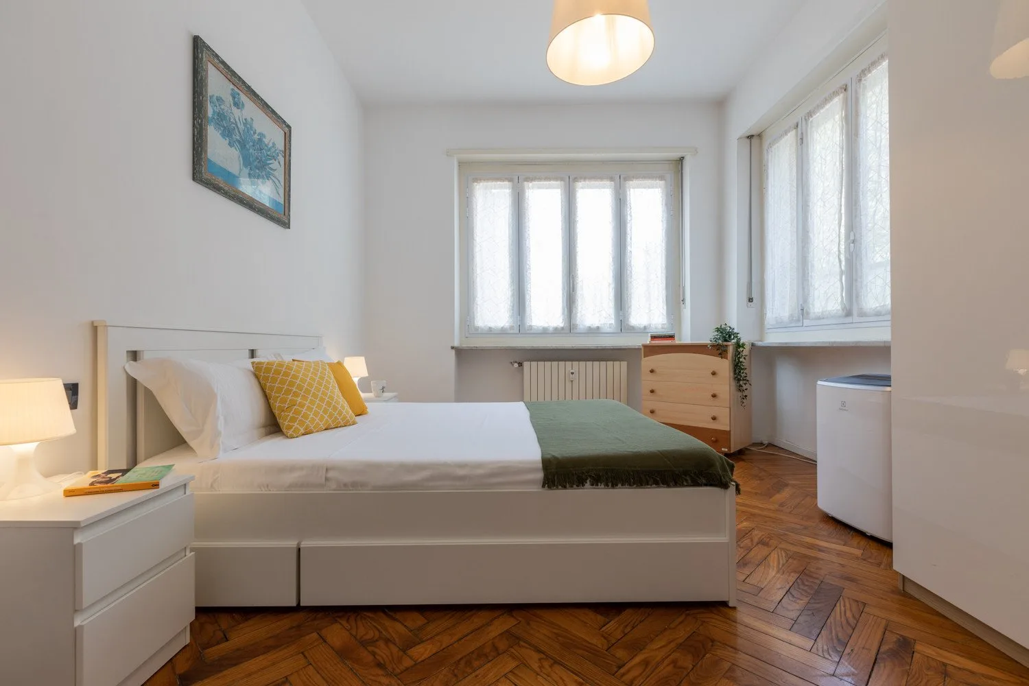 Un dormitorio luminoso con una cama bajo amplias ventanas y suelo de madera.
