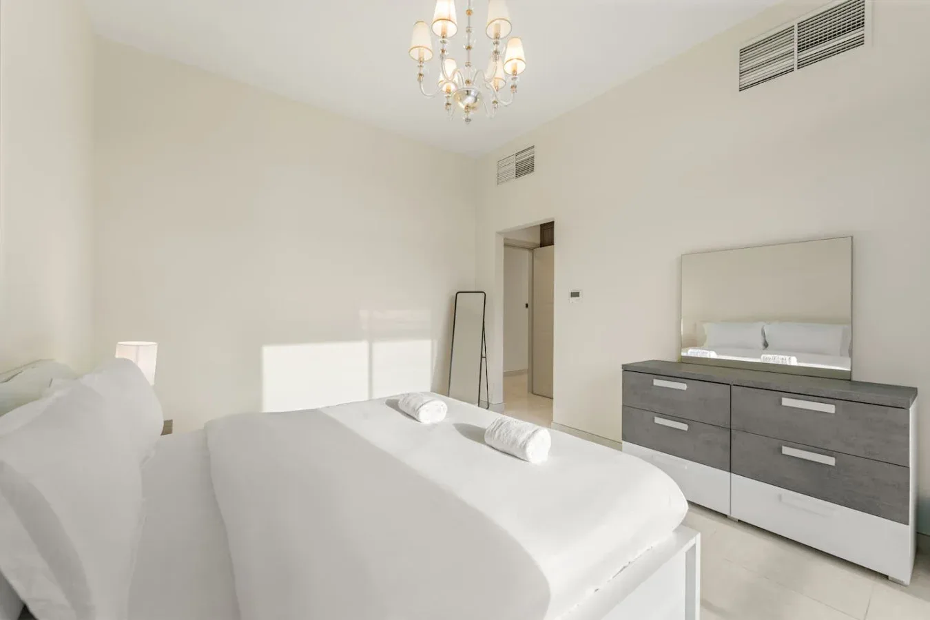 Un dormitorio luminoso con ropa de cama blanca y una cómoda oscura.