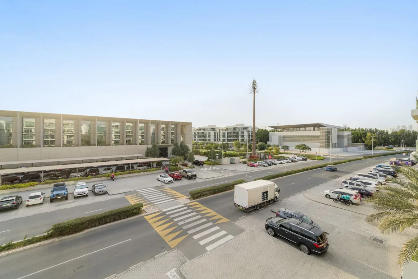 Una calle amplia y una zona de estacionamiento quedan frente a edificios modernos de poca altura.