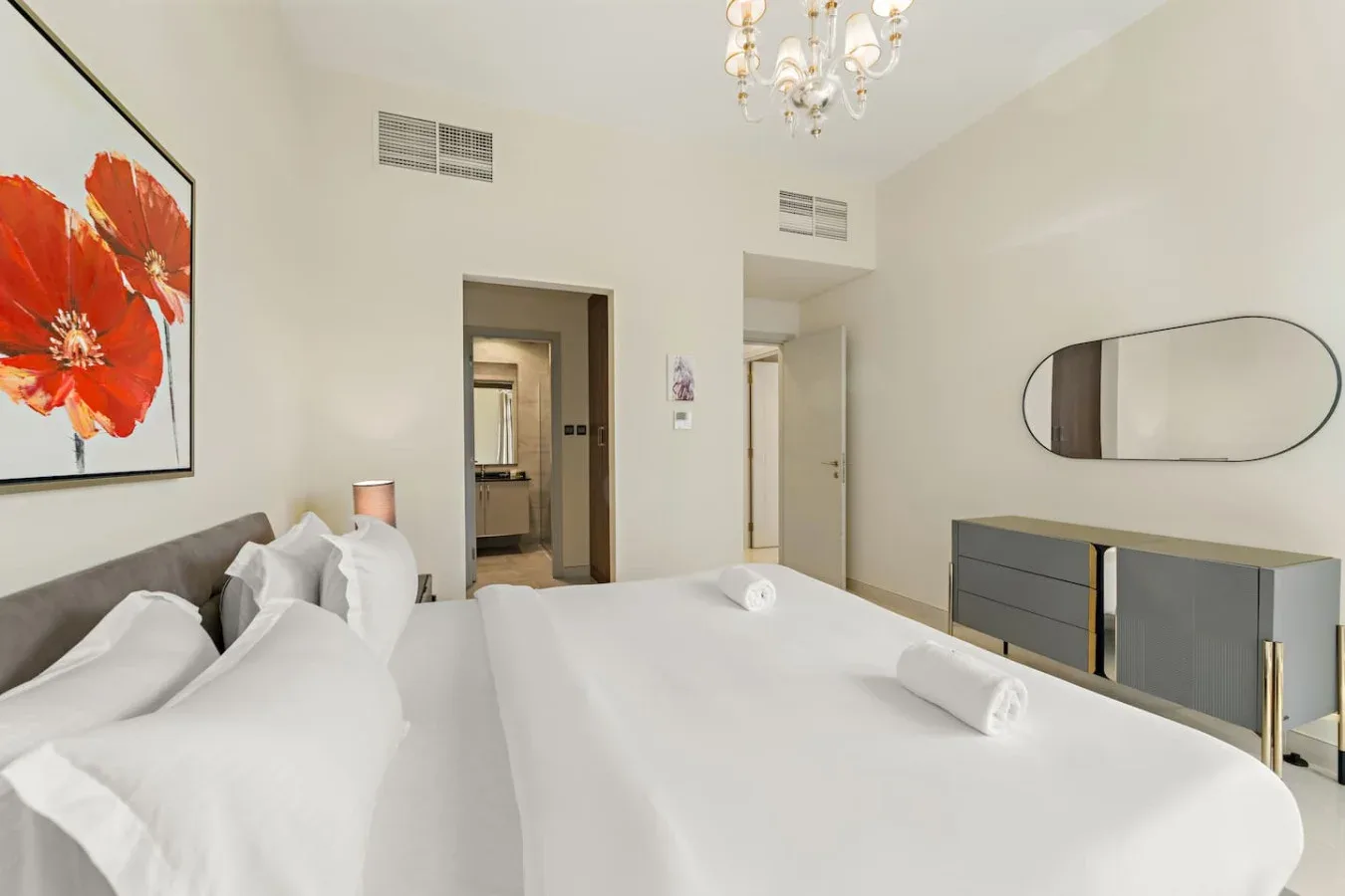 Un dormitorio luminoso con ropa de cama blanca, almohadas y un espejo en la pared.