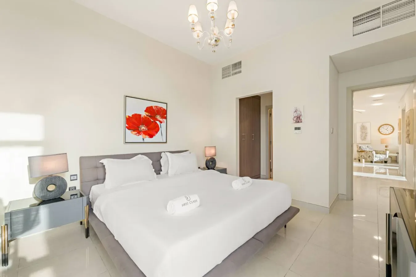 Un dormitorio luminoso tiene una cama grande bajo una lámina floral roja enmarcada.