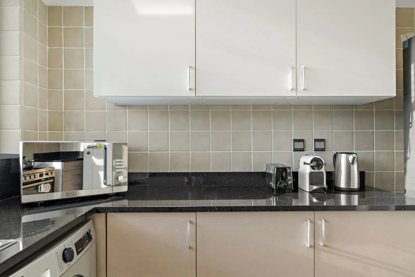 Una encimera de cocina con pequeños electrodomésticos está debajo de armarios blancos.