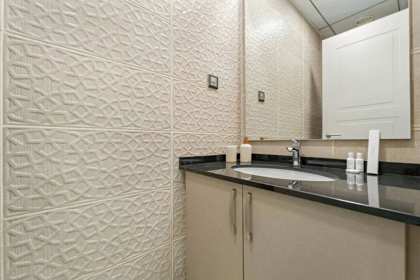 Un tocador de baño con lavabo, espejo y azulejos estampados.