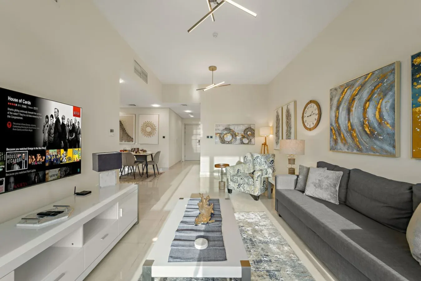 Una sala luminosa con un sofá gris, una mesa de centro y un televisor en la pared.