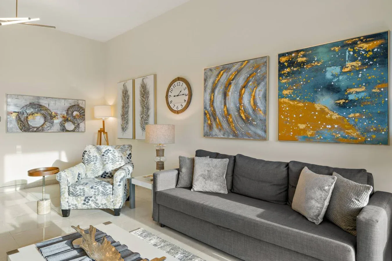 Una sala luminosa con un sofá gris y cuadros coloridos en la pared.