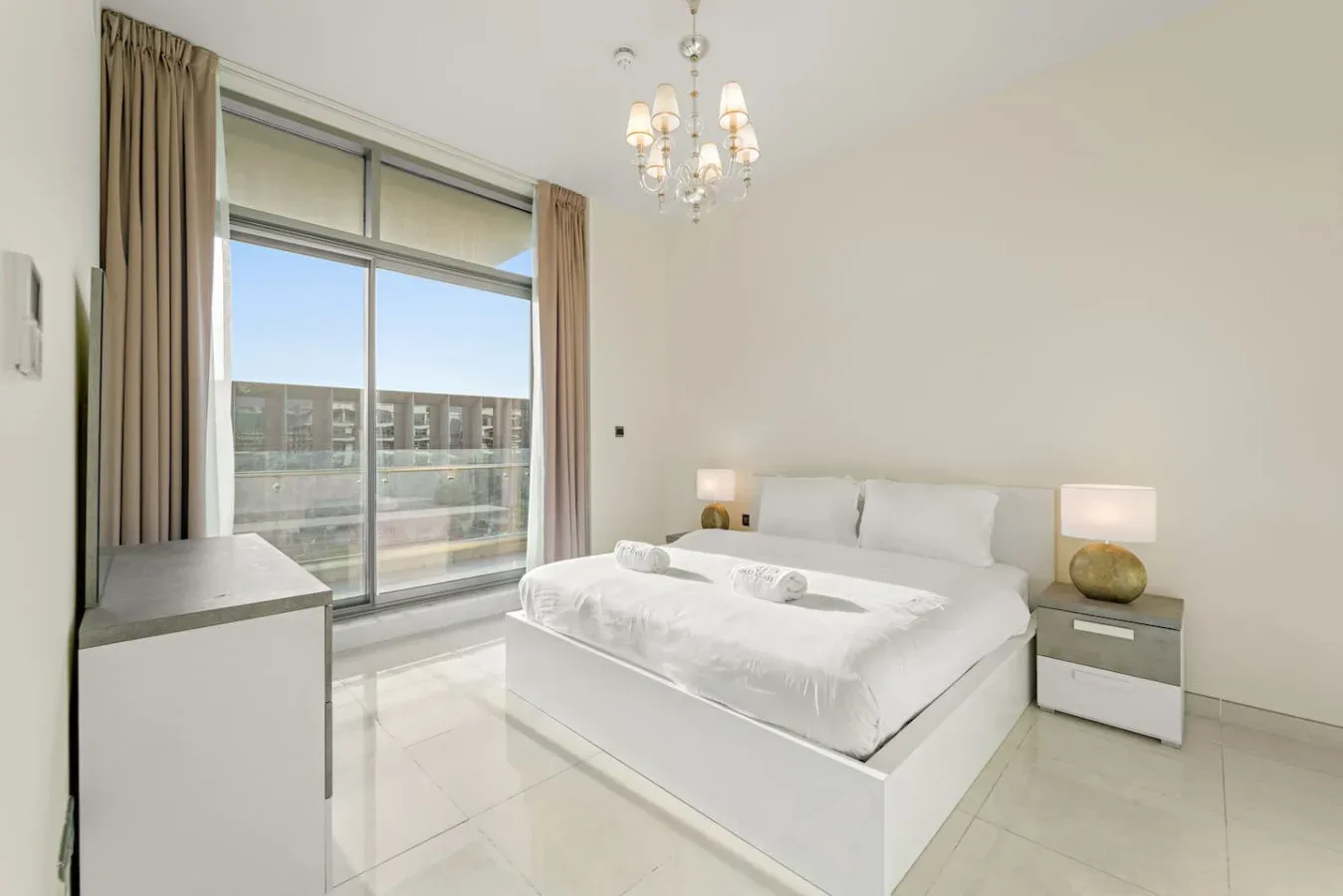 Un dormitorio luminoso con una cama junto a una gran ventana con cortinas.