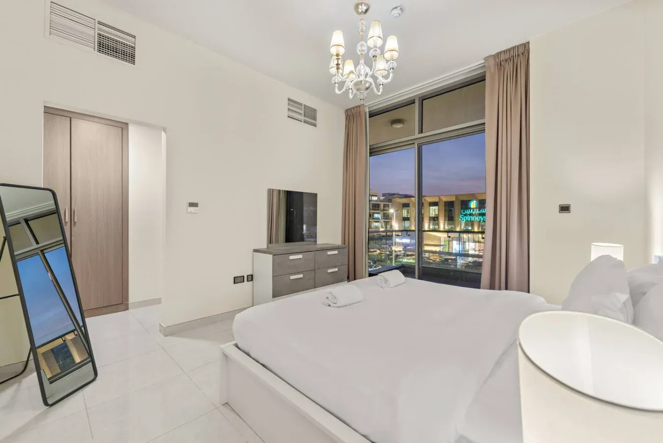 Un dormitorio luminoso con una cama junto a una gran ventana con edificios iluminados al fondo.