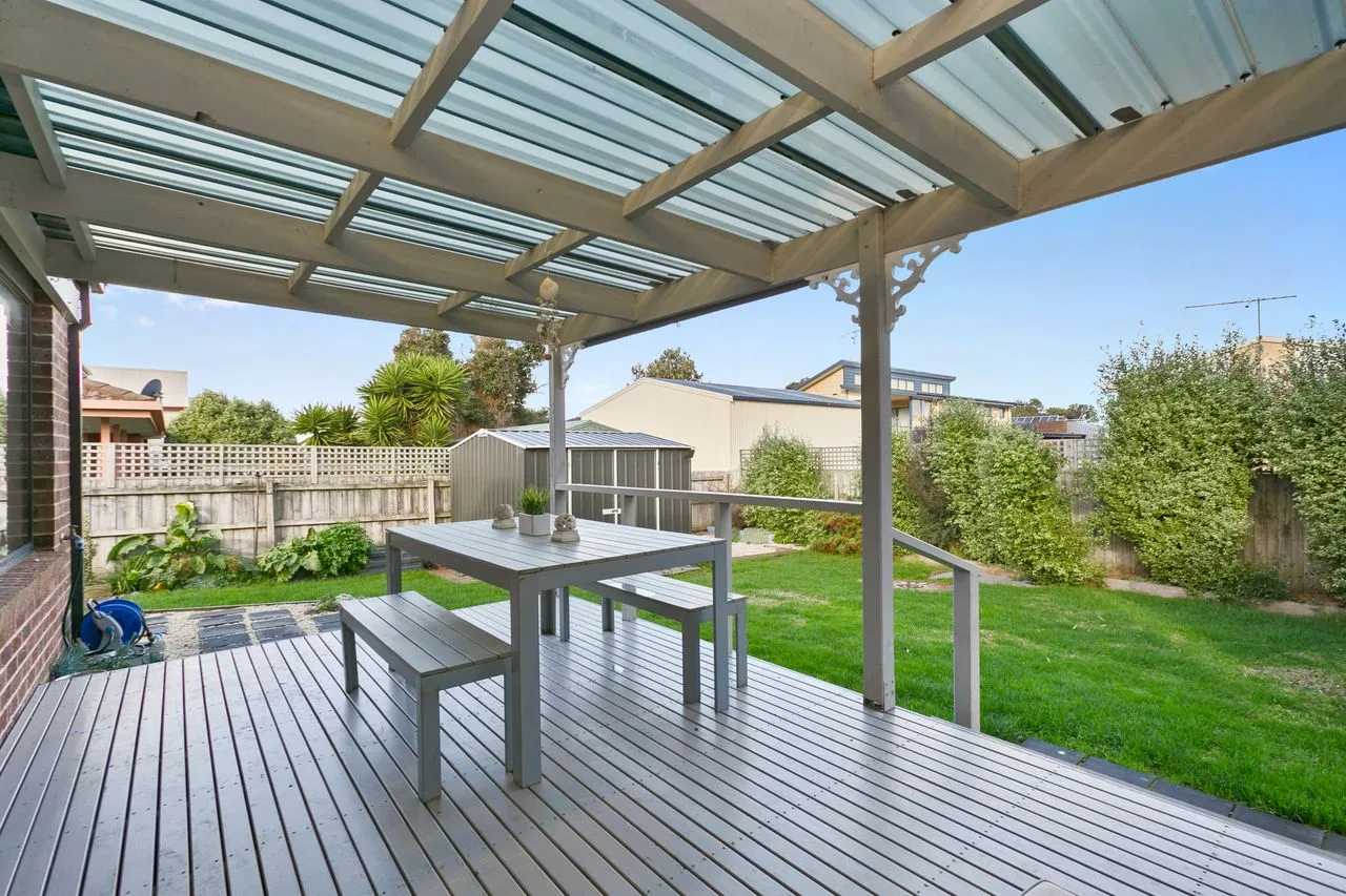A covered outdoor deck with a dining table overlooking a green yard.