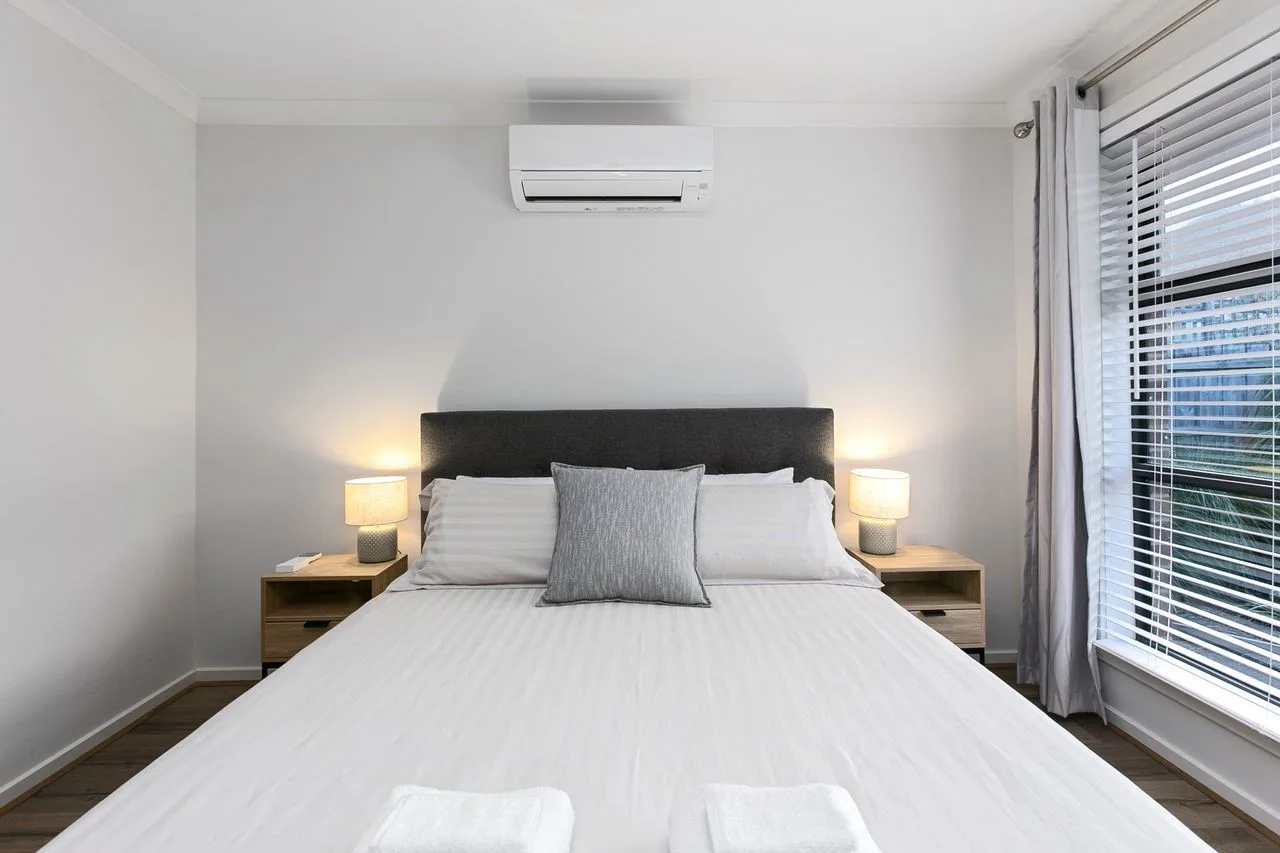 A bright bedroom with a neatly made bed and bedside lamps.