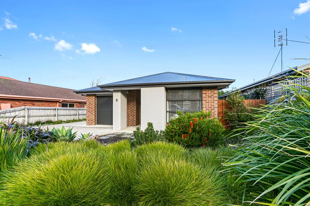A low brick house stands behind a garden of ornamental grasses and shrubs.