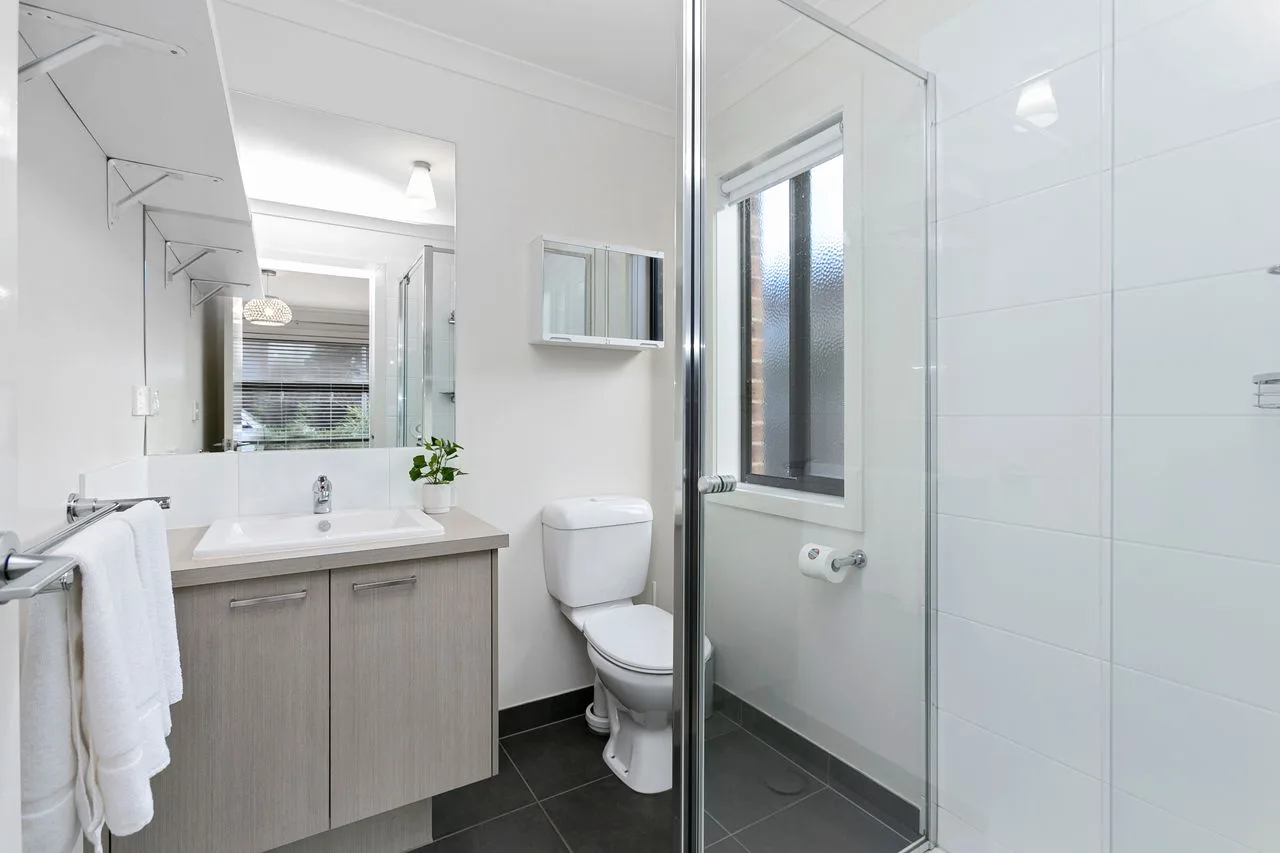 A bright bathroom with a vanity, toilet, and glass shower.